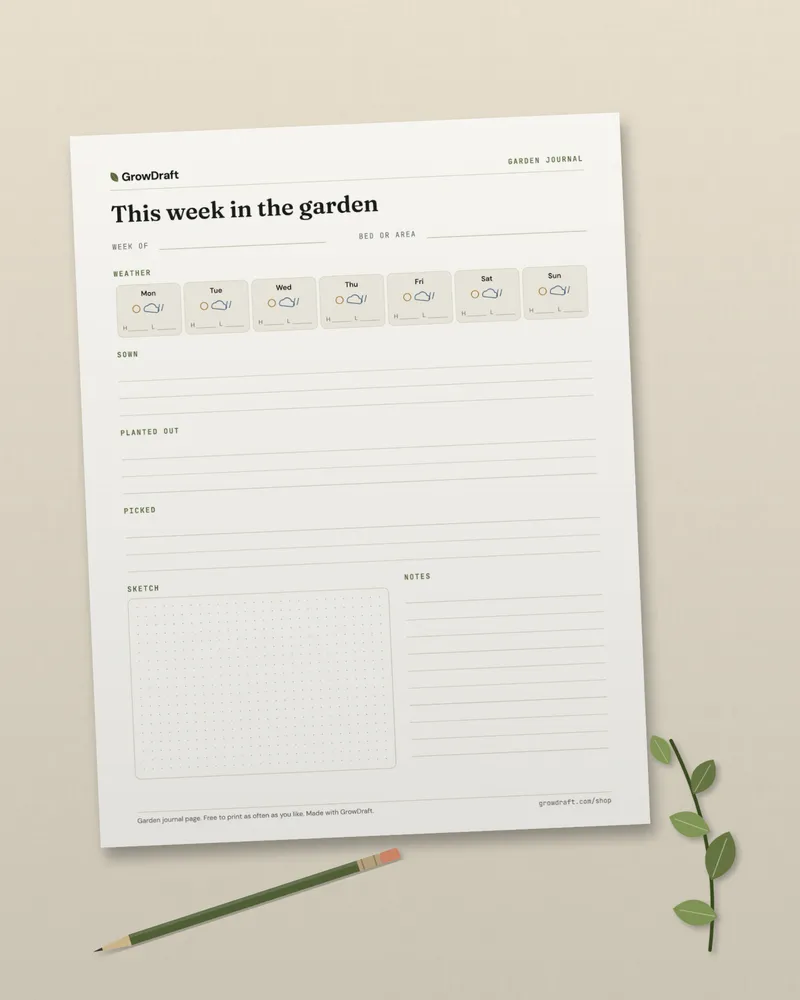 The printed garden journal page on a linen cloth beside a pencil and a sprig of leaves.